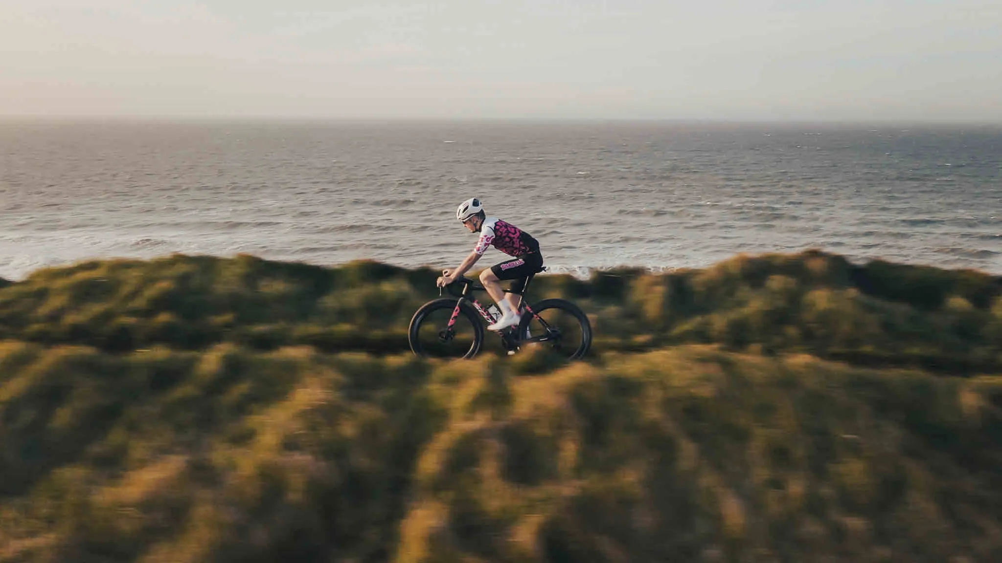 Cycliste en maillot Chasse Patate × Barbeuk sur une falaise face à la mer